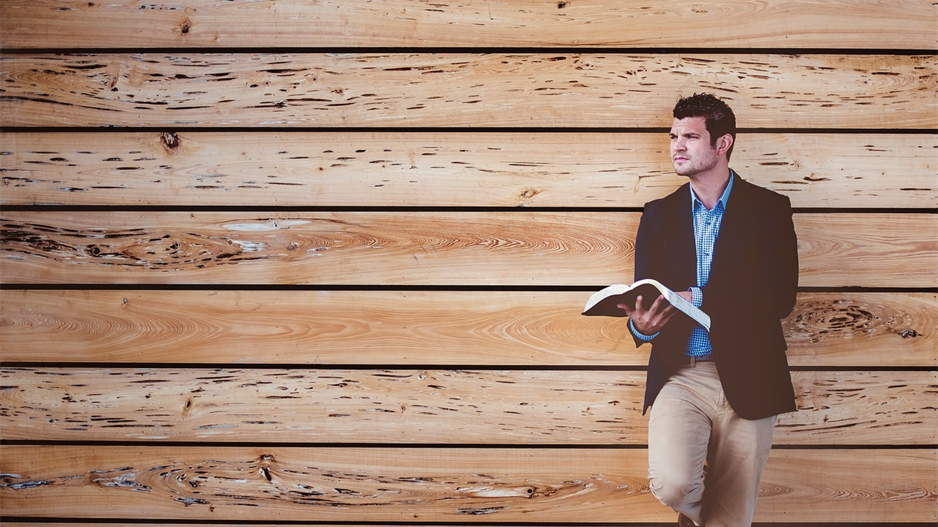 Hombre leyendo la Biblia apoyado en una pared de madera