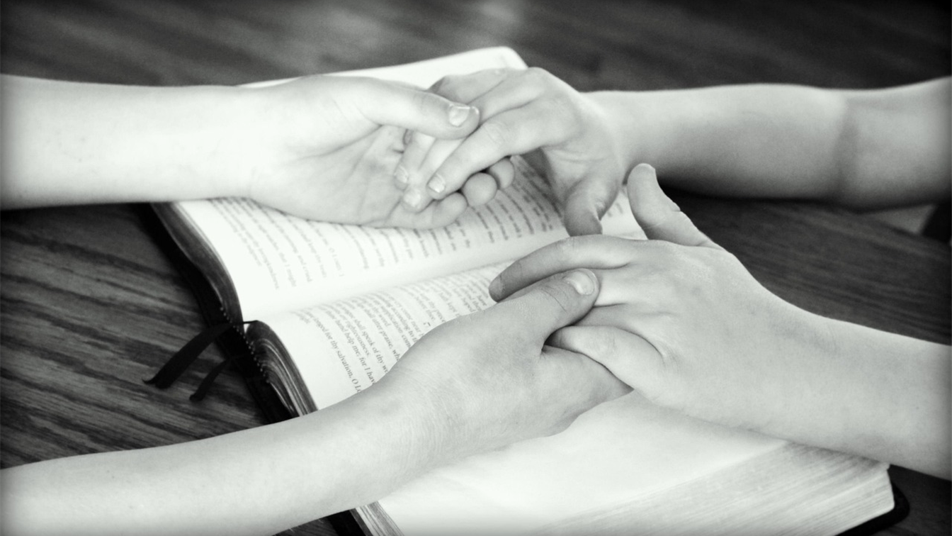 Manos entrelazadas sobre una Biblia abierta