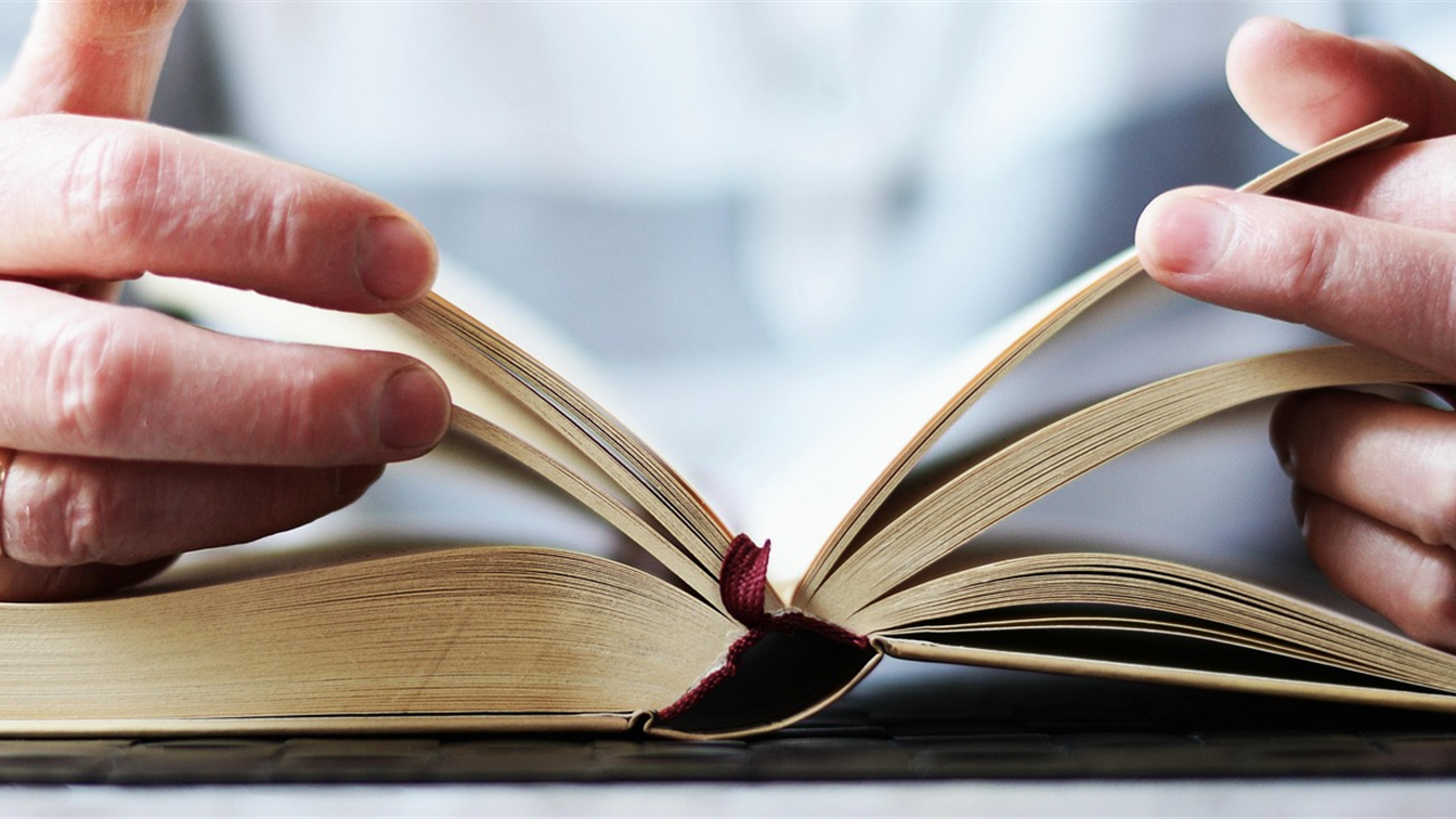 Manos abriendo un libro antiguo sobre una mesa