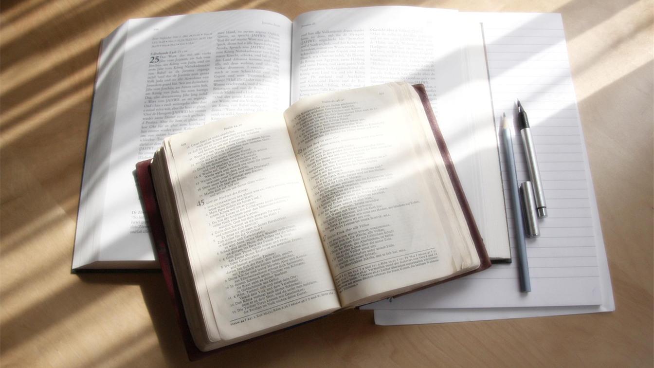 Dos biblias abiertas sobre una mesa con luz natural y un cuaderno