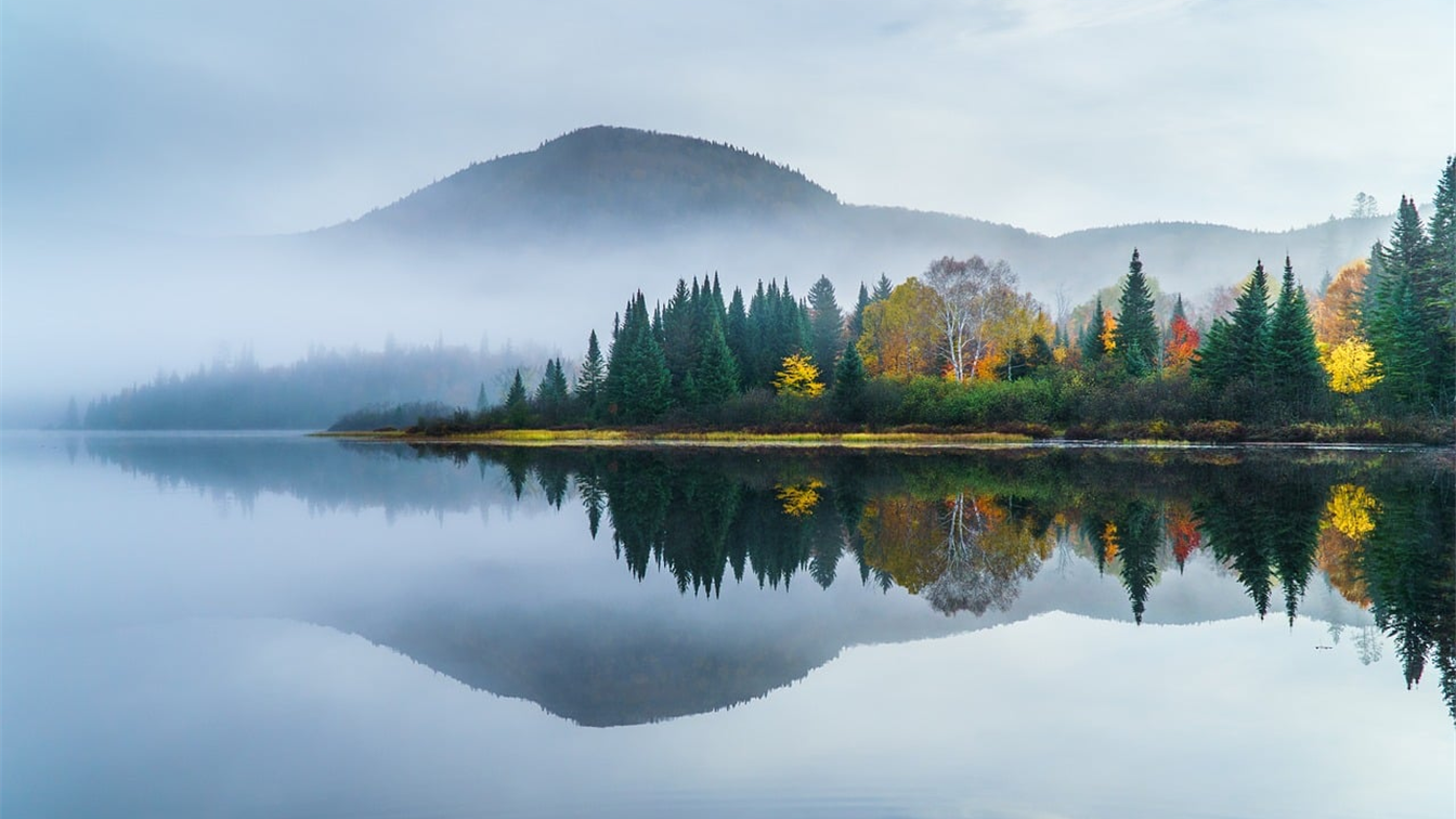 Lago en calma rodeado de montanas con niebla y arboles de otono