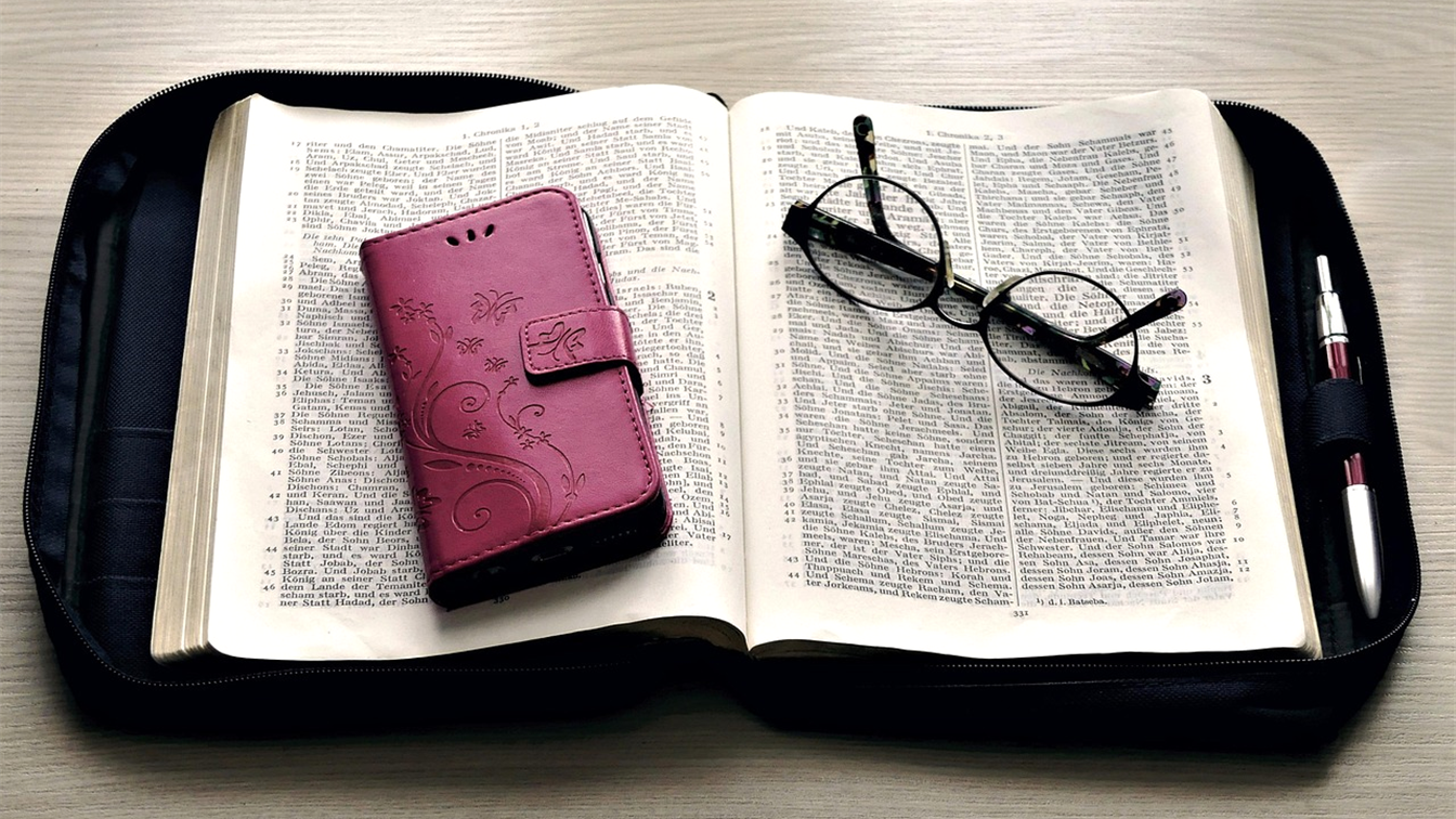Biblia abierta con gafas y un movil sobre una funda de transporte