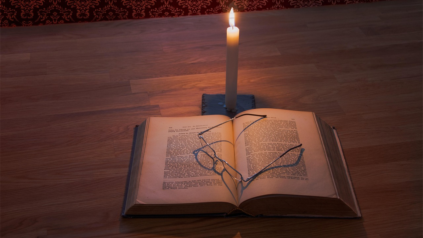 Biblia abierta con gafas y una vela encendida sobre una mesa de madera