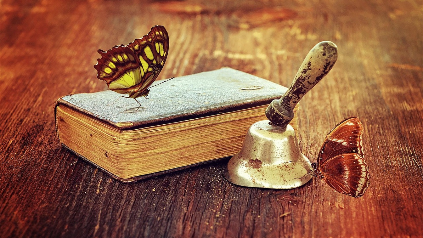 Libro antiguo con una campana y mariposas sobre una mesa de madera