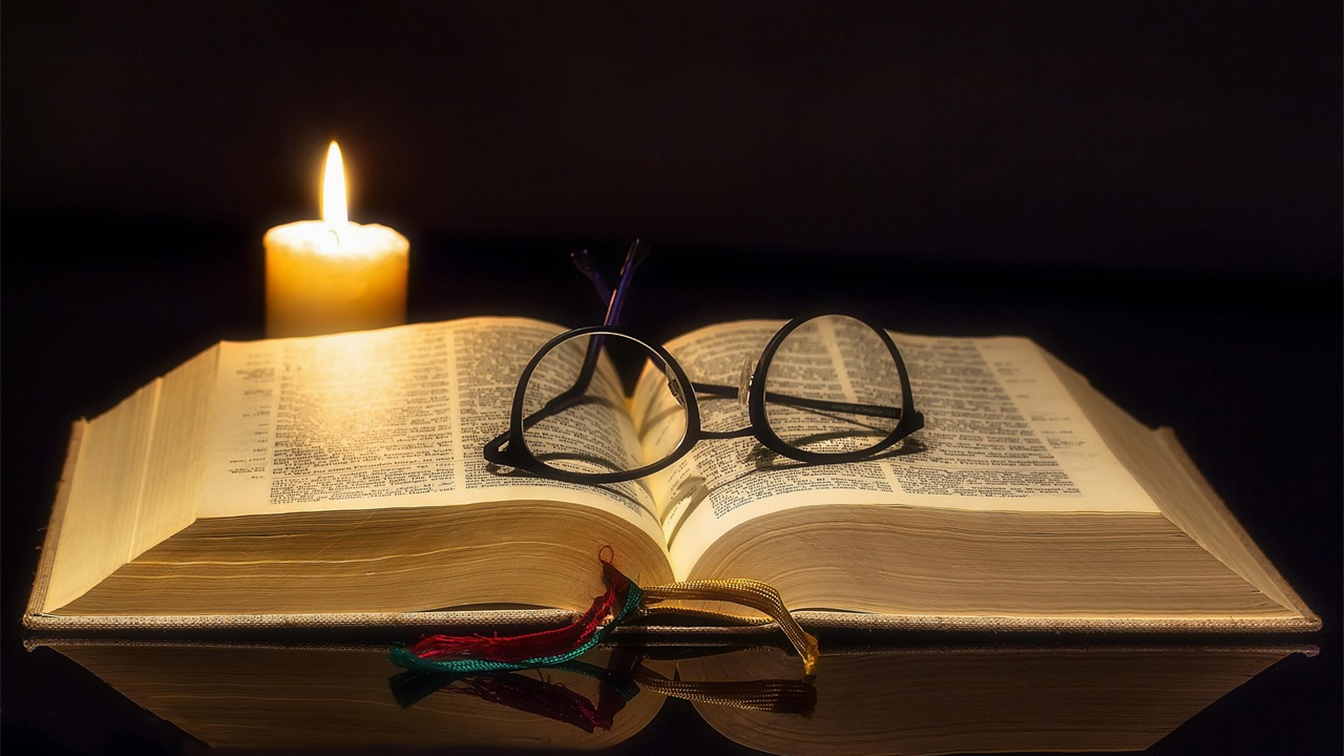 Biblia abierta con vela y gafas